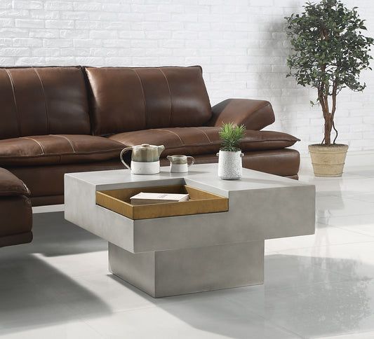 A modern living room with a brown leather sofa, the Kailano Weathered Table in gray featuring an open storage compartment and a potted plant on top, plus a larger potted plant on the floor against a white brick wall.