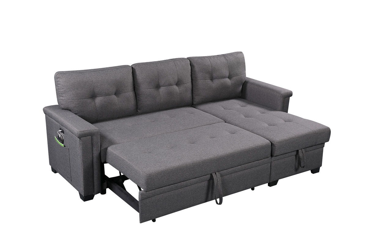 The Ashlyn Reversible Sleeper Sectional Sofa with storage chaise, USB charging ports, and pocket is shown extended as a bed against a white background, highlighting its gray upholstery and tufted cushions.