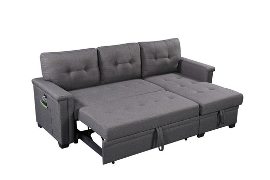 The Ashlyn Reversible Sleeper Sectional Sofa with storage chaise, USB charging ports, and pocket is shown extended as a bed against a white background, highlighting its gray upholstery and tufted cushions.