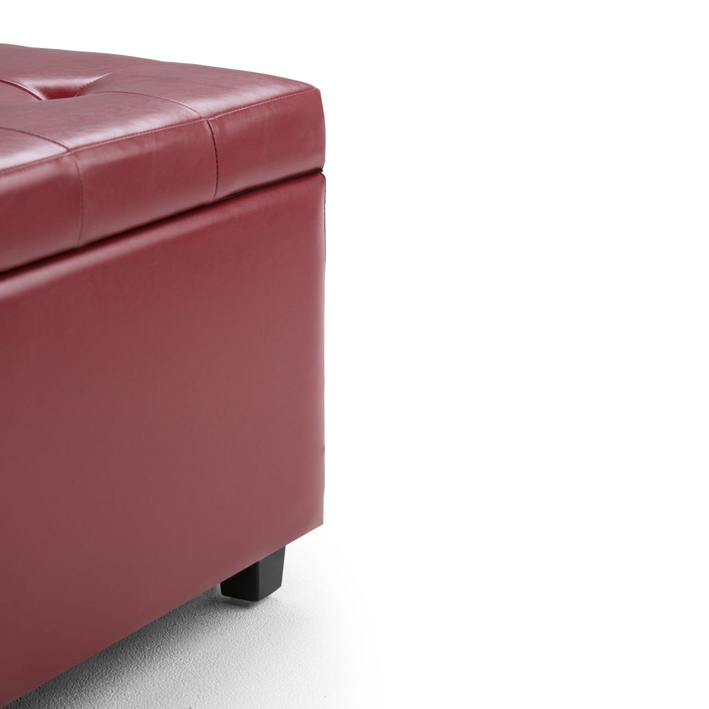 Close-up of the corner of the Cosmopolitan - Upholstered Storage Ottoman in red with dark wooden legs on a white background. The ottoman showcases a smooth, tufted surface and offers hidden storage.