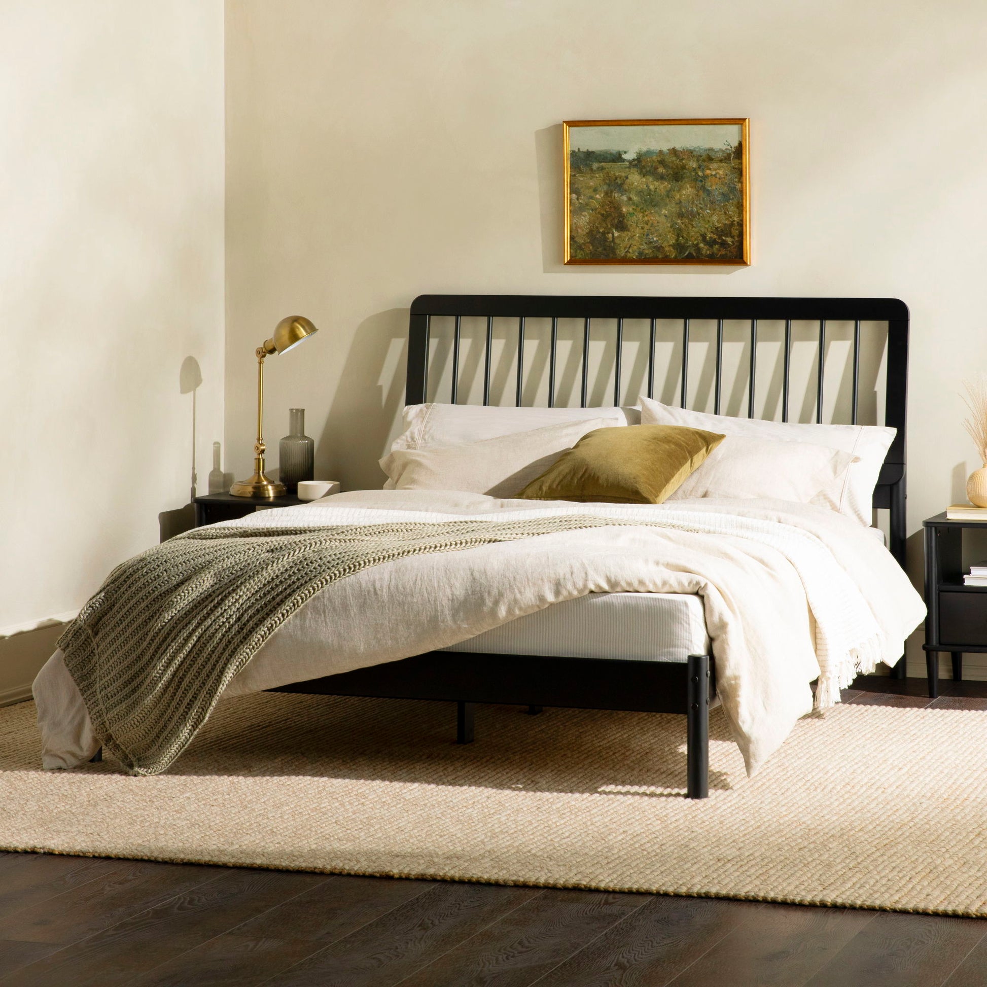 A modern bedroom features the Mid-Century Modern Solid Wood Spindle Bed, styled with beige bedding, a green throw blanket, and a gold accent pillow. Above hangs a framed landscape painting; nightstands and lamps flank each side.