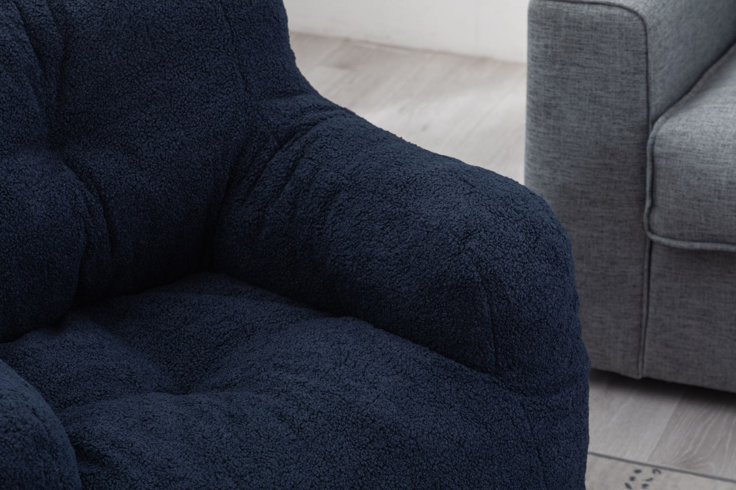Close-up of the Soft Teddy Fabric Tufted Foam Bean Bag Chair with plush, textured teddy fabric in dark blue, placed beside a gray sofa on a light wood floor.