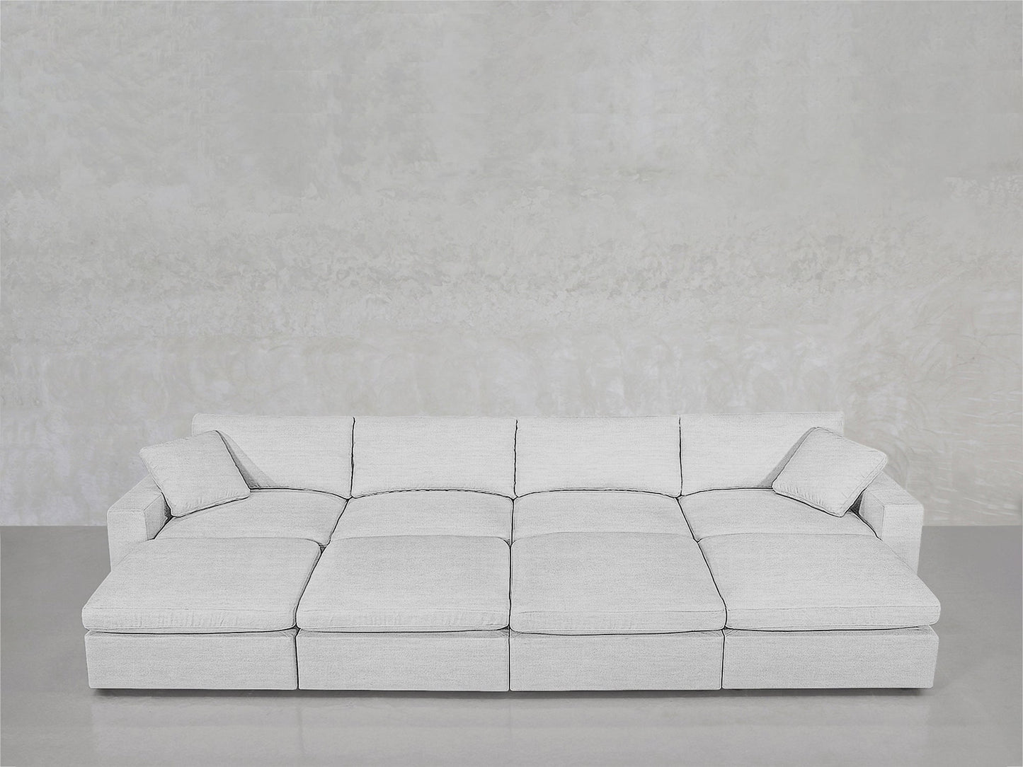 An 8-Seat Modular Daybed in light gray with matching pillows, arranged against a textured light gray wall and smooth gray floor.