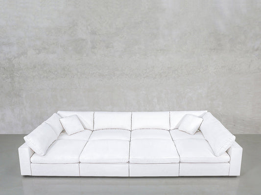 The 8-Seat Modular Pit is a large, modern white sofa featuring wide seats, square armrests, and two matching white cushions, set against a plain light gray wall and smooth concrete floor.