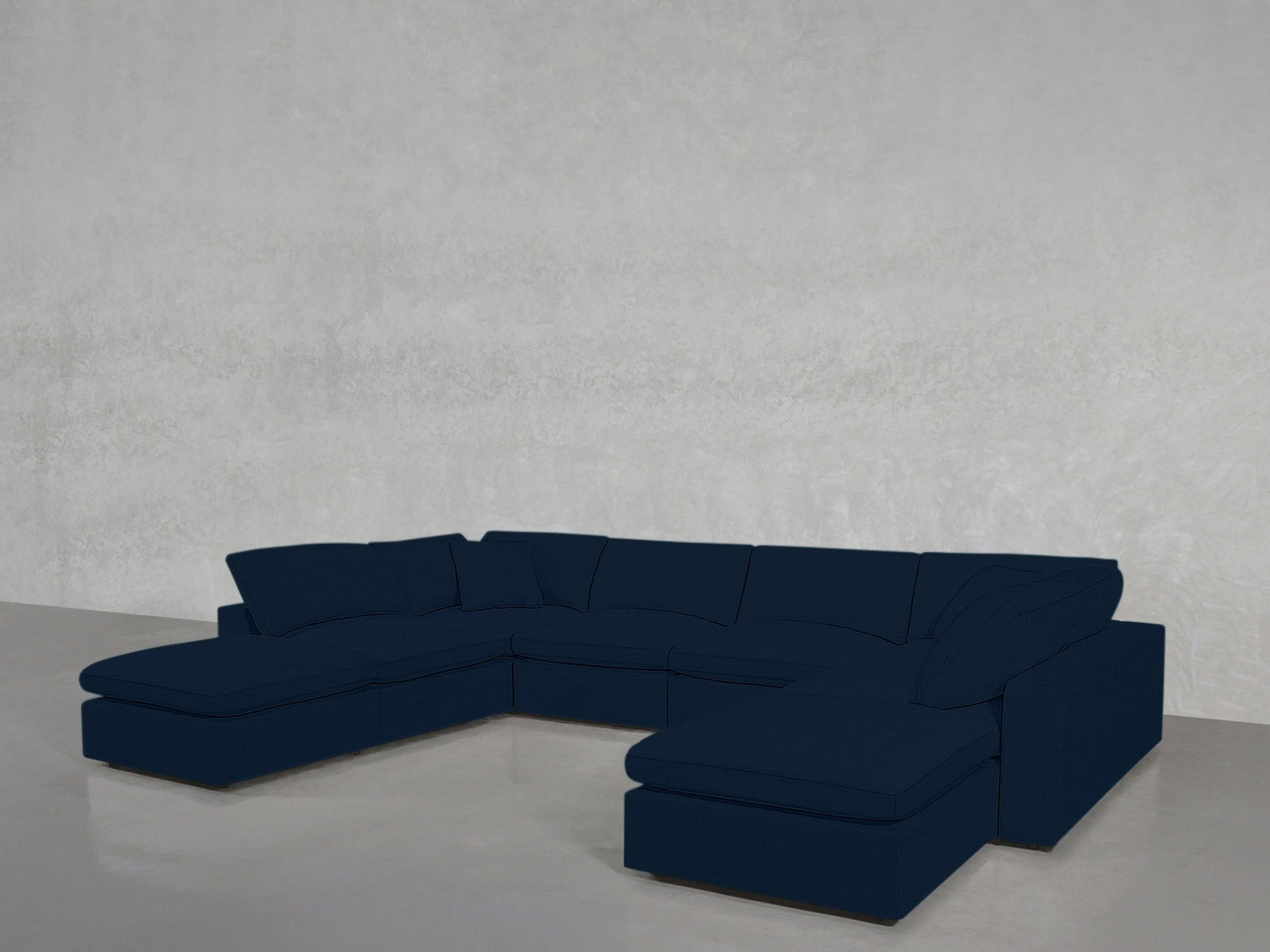 An 8-Seat Modular Double Lounger U-Sectional in dark blue with cushions sits in a minimalist room featuring light gray walls and a polished concrete floor.