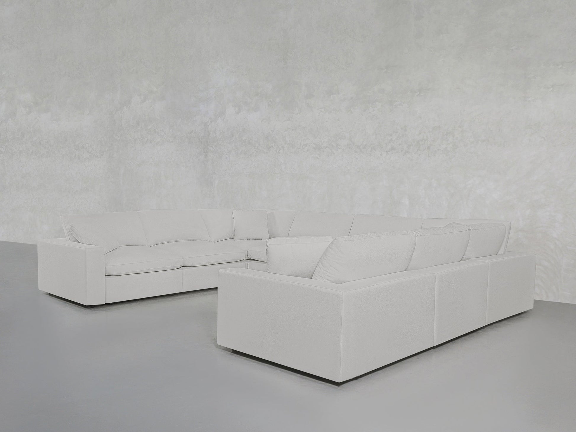 The 8-Seat Modular U-Sectional, featuring clean lines and plush cushions in light gray, is set against a minimalist, textured light gray wall and floor.