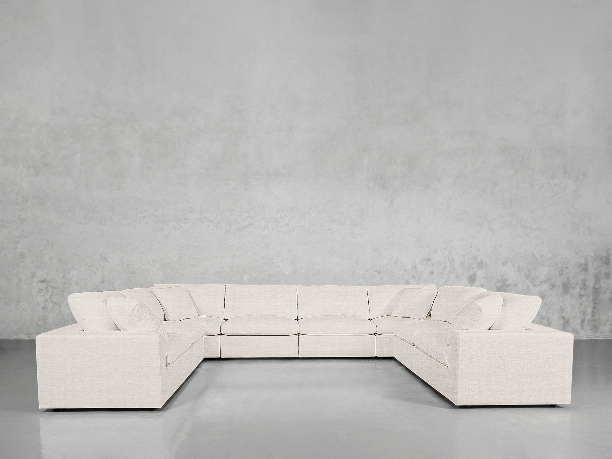 An 8-Seat Modular U-Sectional with a modern white design and plush cushions is placed against a light gray wall in a minimal room featuring a shiny gray floor.