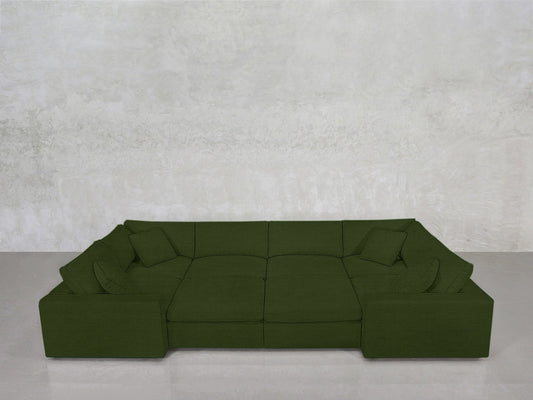 The 8-Seat Modular Closed Pit, in deep green with wide seats and matching pillows, sits before a smooth, light gray textured wall on a pale floor.