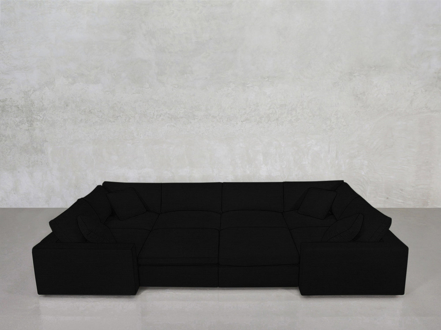 An 8-Seat Modular Closed Pit in black, featuring four matching cushions, sits against a light gray textured wall on a smooth, light floor.