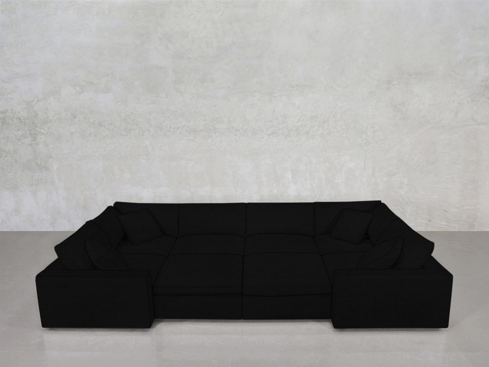 An 8-Seat Modular Closed Pit in black, featuring four matching cushions, sits against a light gray textured wall on a smooth, light floor.