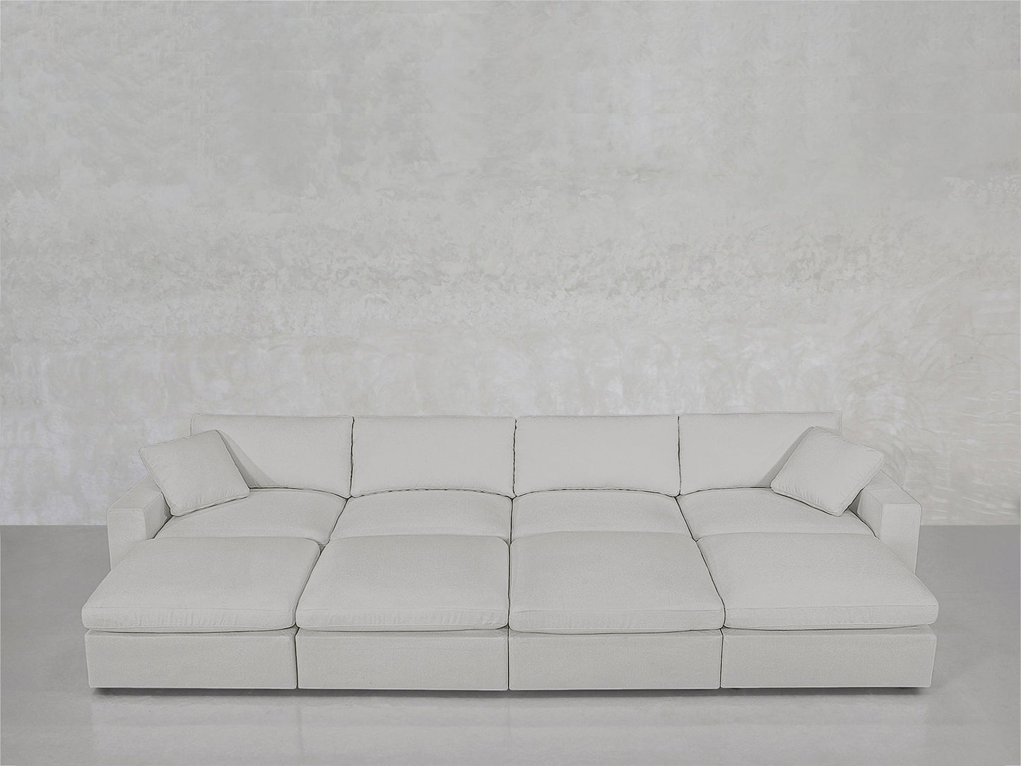The 8-Seat Modular Daybed in light gray features wide seats and two matching throw pillows, set against a textured pale gray wall atop a smooth, light-colored floor.