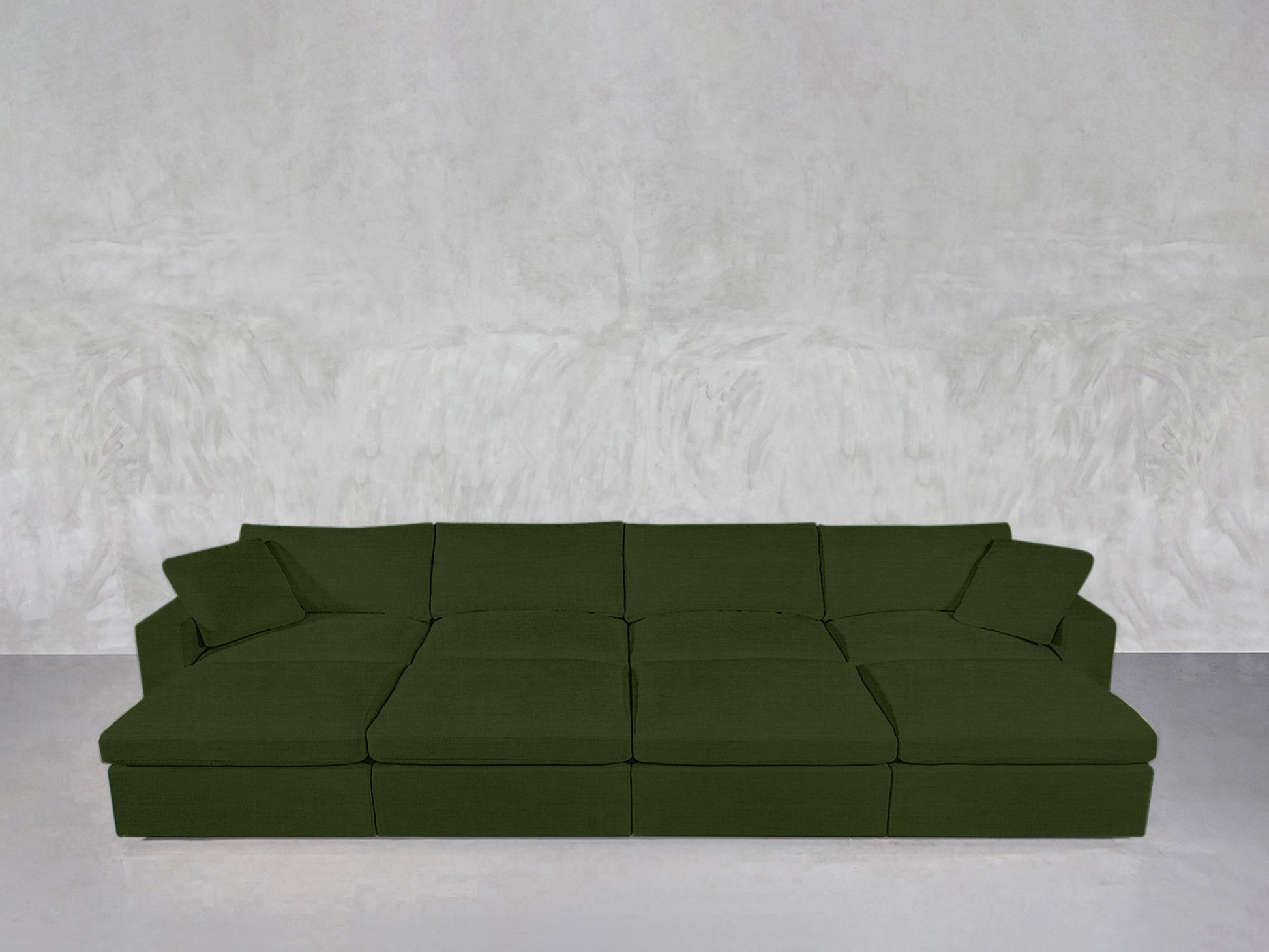 An 8-Seat Modular Daybed in modern green with two matching throw pillows sits against a textured light gray wall on a smooth, light gray floor.