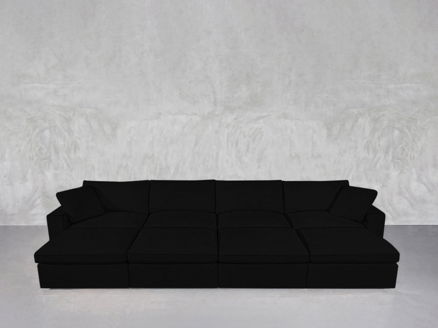 An 8-Seat Modular Daybed in modern black with wide seats and cushions sits against a light gray textured wall and floor in a minimalist room.