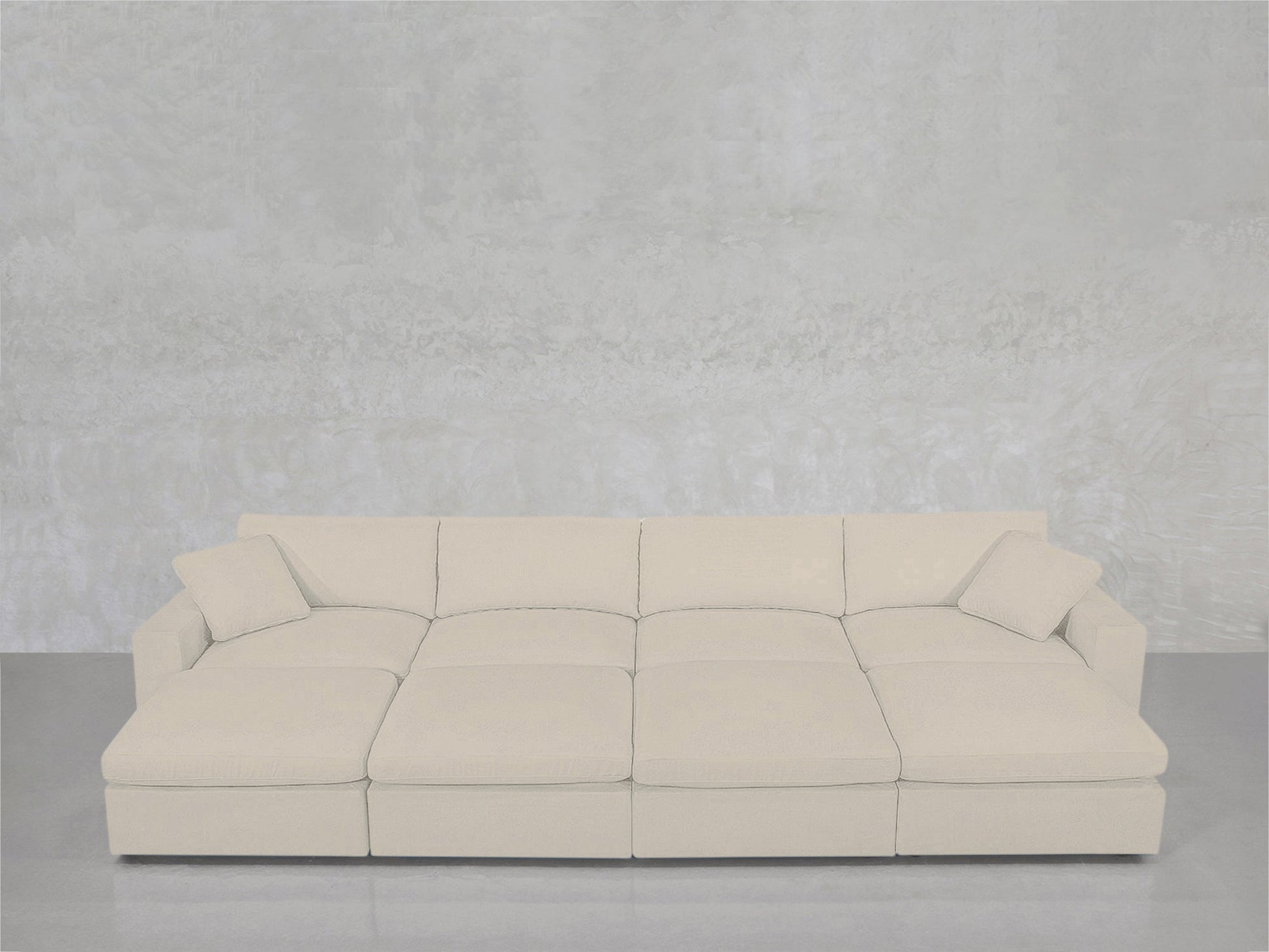 The 8-Seat Modular Daybed in light beige, featuring three seat sections and two matching square cushions, is set against a textured light gray wall on a smooth floor.