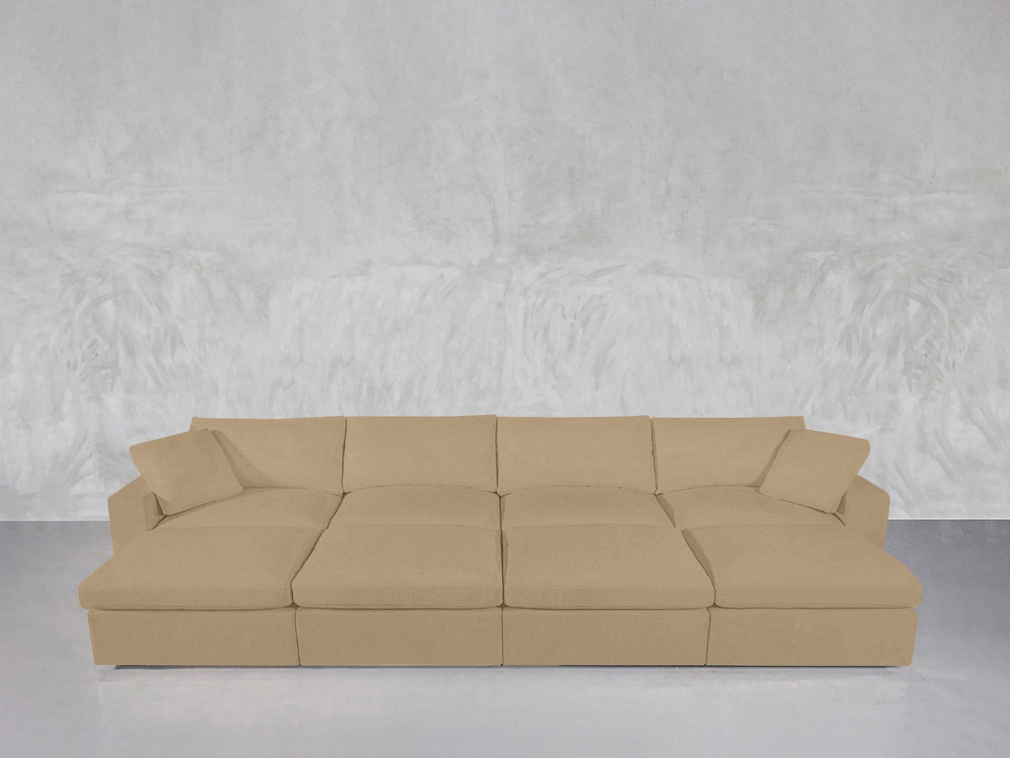 An 8-Seat Modular Daybed in beige with four matching pillows sits on a light-colored floor in front of a textured light gray wall.