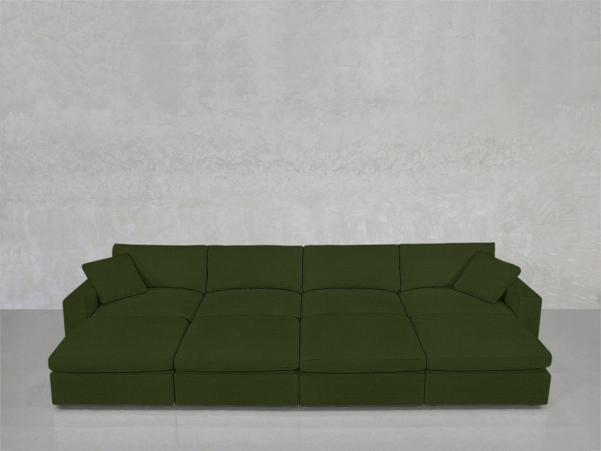 An 8-Seat Modular Daybed in dark green with two matching cushions is placed against a light gray textured wall on a shiny, reflective floor.