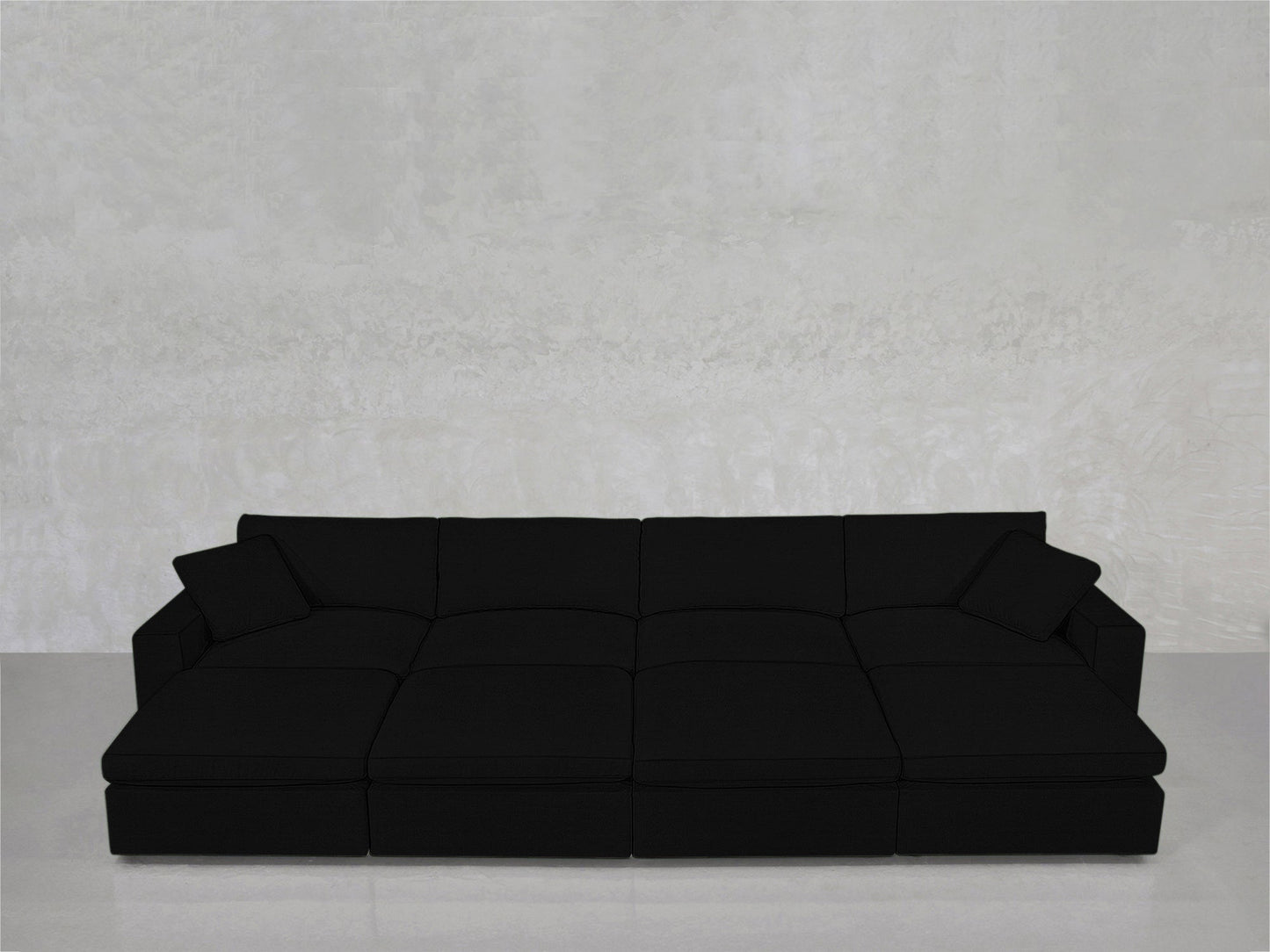 An 8-Seat Modular Daybed in modern black, with two matching cushions, sits against a textured light gray wall on a shiny, light-colored floor.