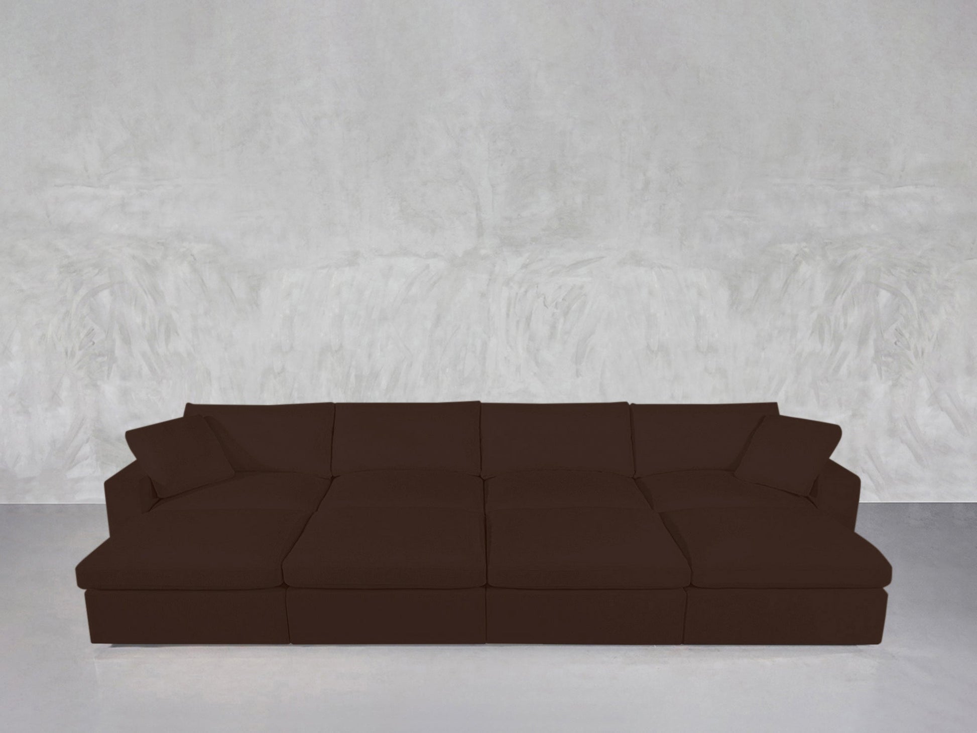 An 8-Seat Modular Daybed with cushions and armrests is placed against a light gray, textured wall on a smooth, light-colored floor.
