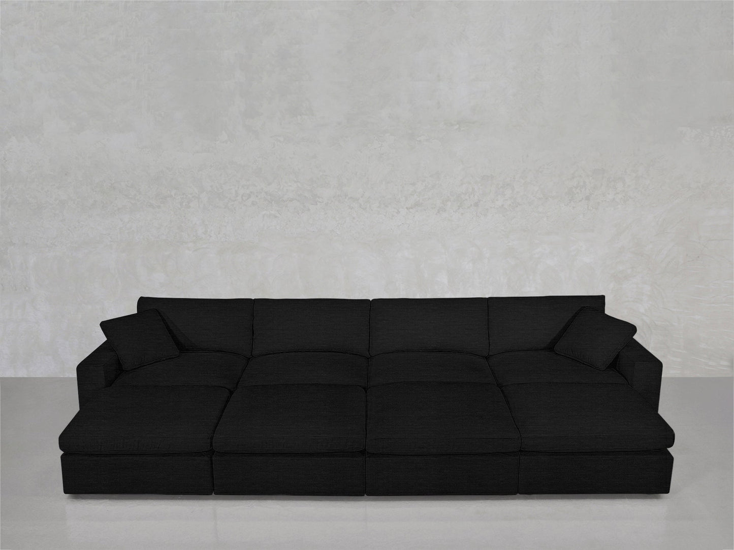 An 8-Seat Modular Daybed with two matching cushions sits against a plain light gray textured wall and glossy floor.