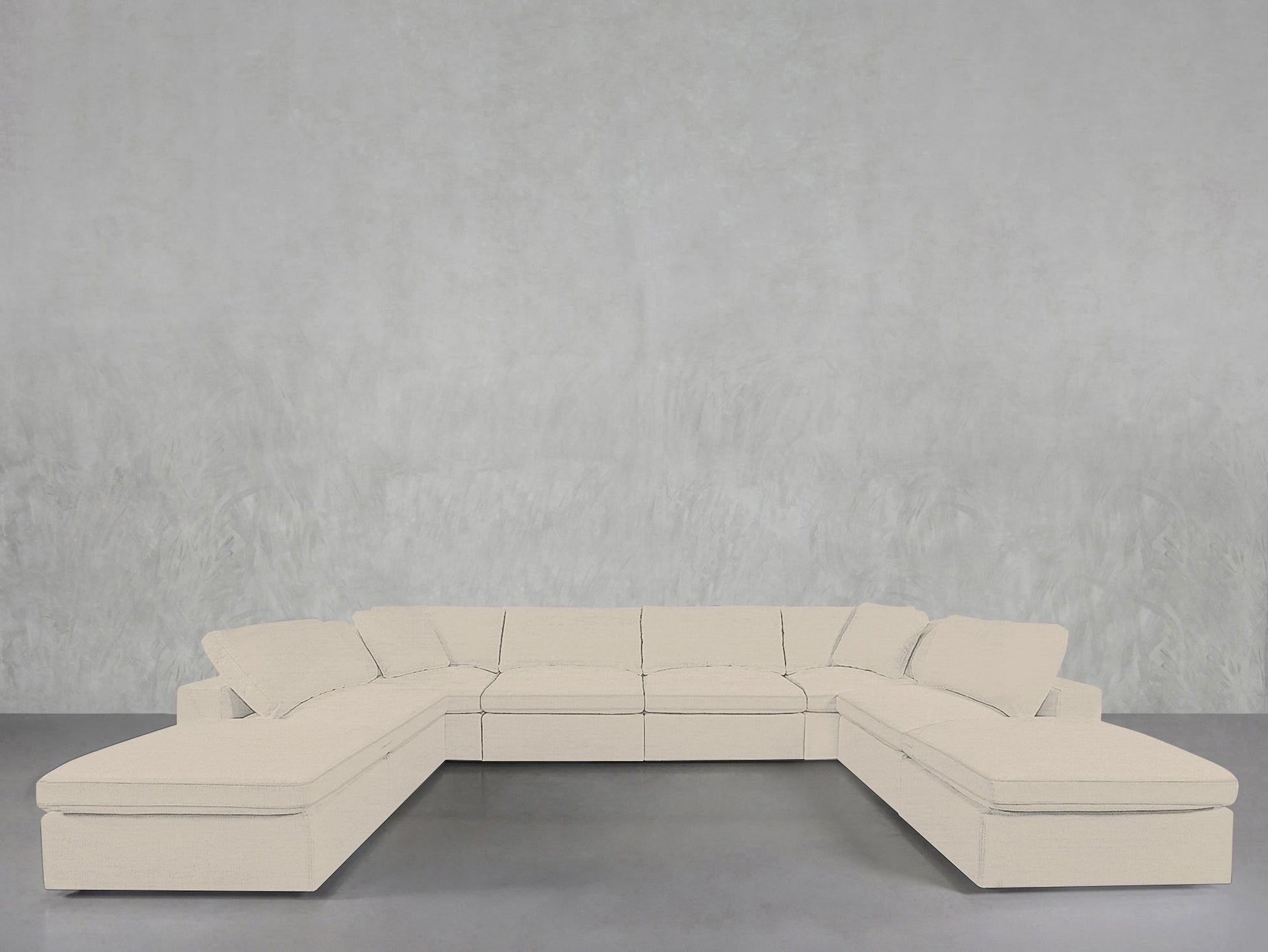 An 8-Seat Modular Double Lounger U-Sectional in light beige with wide cushions is set against a plain, light gray textured wall on a smooth gray floor.