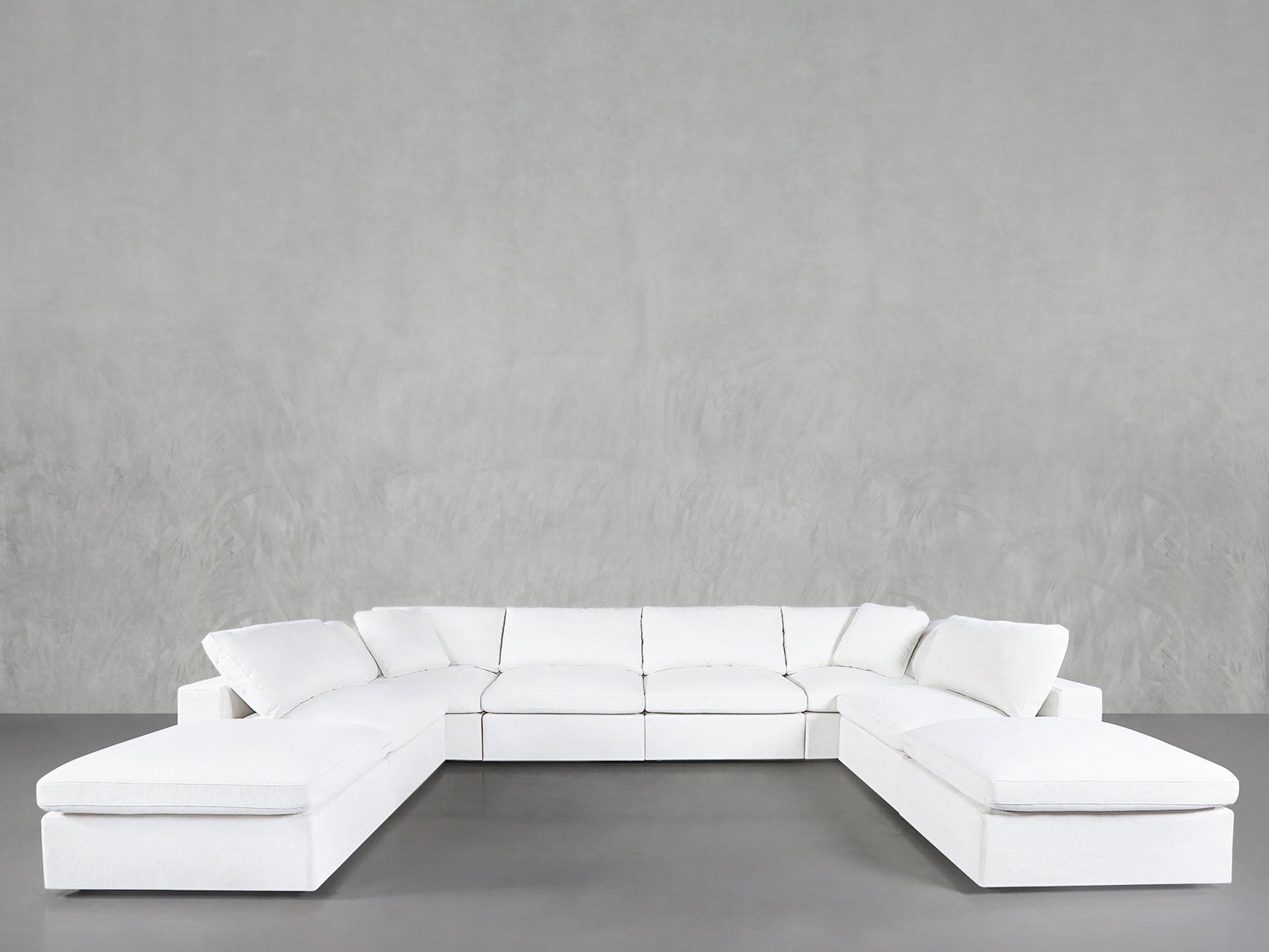 The 8-Seat Modular Double Lounger U-Sectional, in white with plush cushions, is arranged against a plain light gray wall in a minimalist room featuring a smooth gray floor.