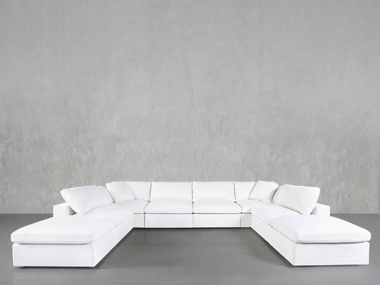 The 8-Seat Modular Double Lounger U-Sectional, in white with plush cushions, is arranged against a plain light gray wall in a minimalist room featuring a smooth gray floor.
