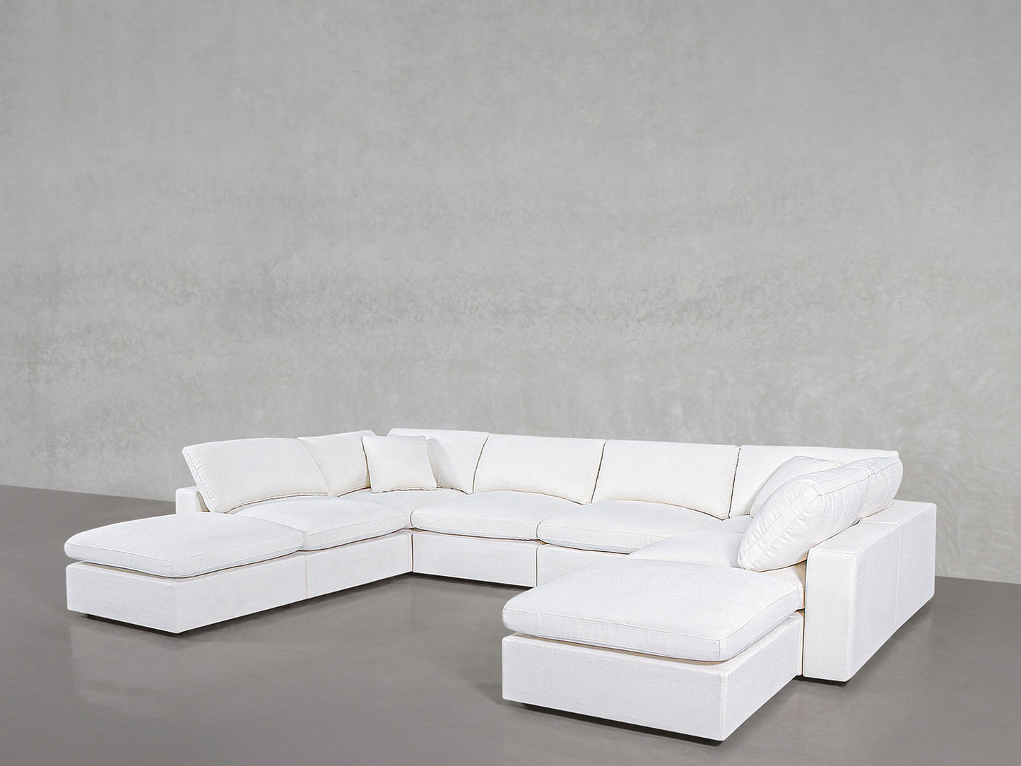 The 8-Seat Modular Double Lounger U-Sectional, a spacious and modern white sofa with plush cushions, is arranged in a U-shape against a plain light gray wall and smooth gray floor.