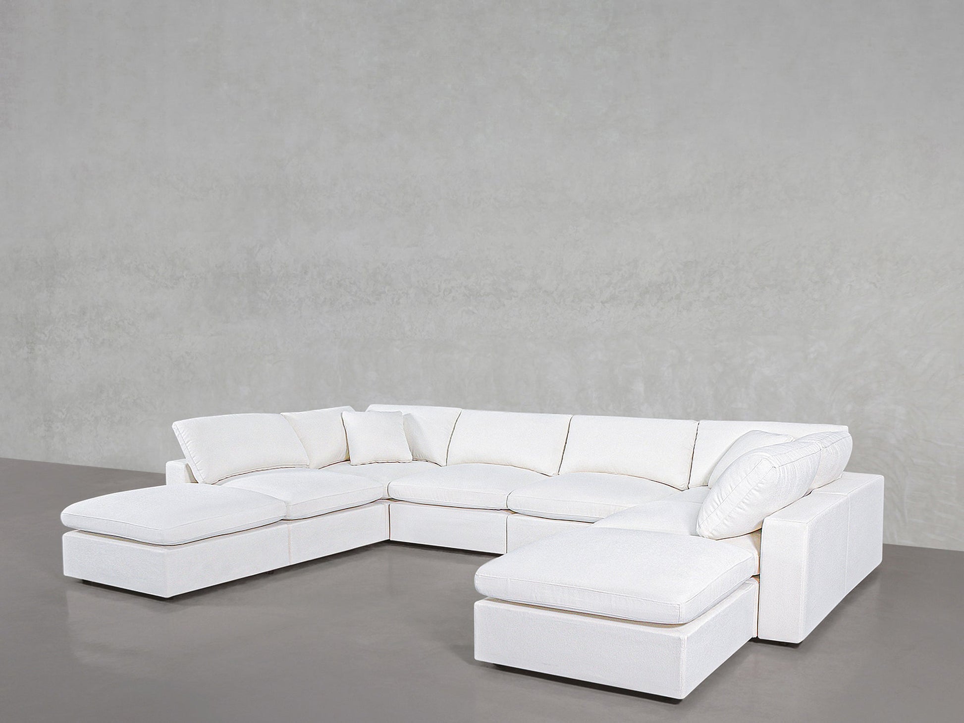 The 8-Seat Modular Double Lounger U-Sectional, a spacious and modern white sofa with plush cushions, is arranged in a U-shape against a plain light gray wall and smooth gray floor.
