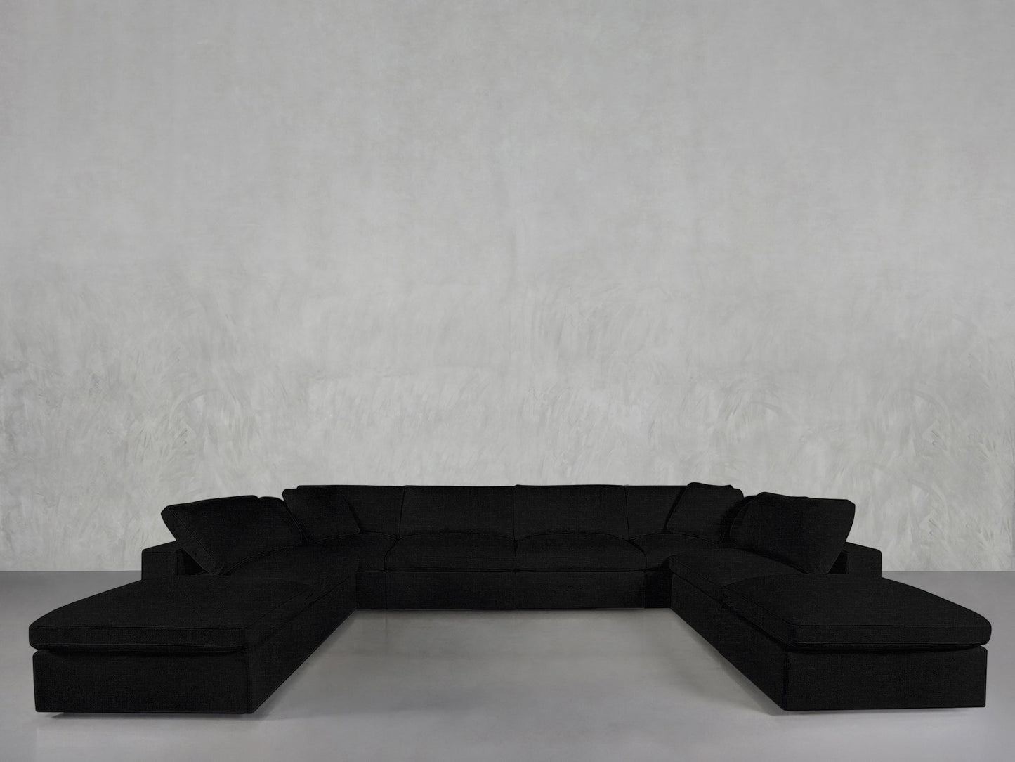 The 8-Seat Modular Double Lounger U-Sectional, a sleek black modern sofa with two chaise lounges, is arranged against a plain light gray wall and light floor in a minimalist setting.