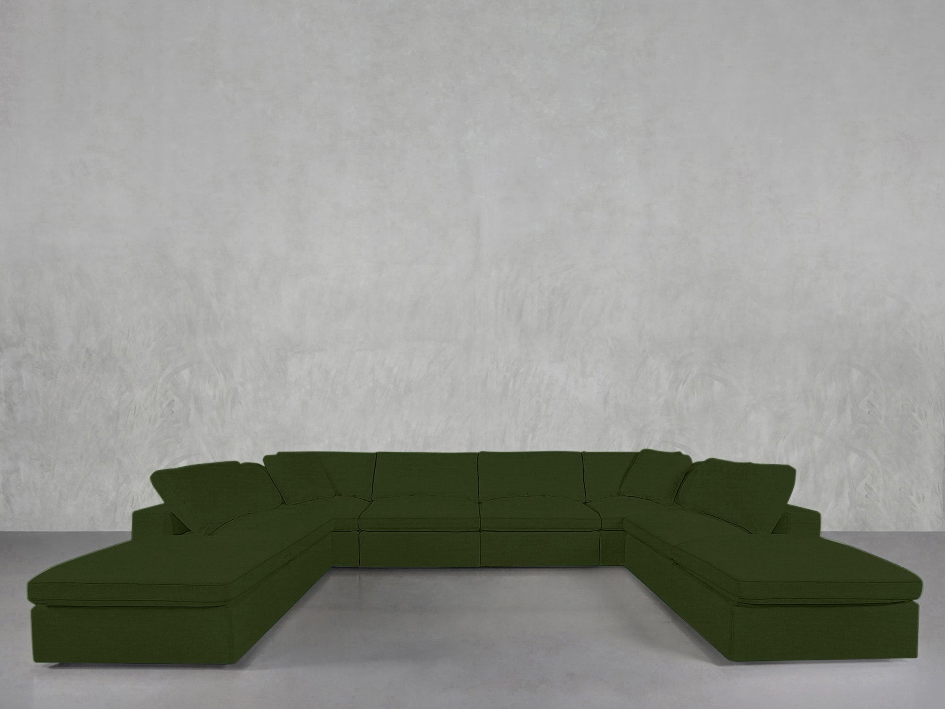 An 8-Seat Modular Double Lounger U-Sectional in dark green is placed against a plain light gray wall on a polished concrete floor, featuring chaise lounges on both ends for modern comfort.