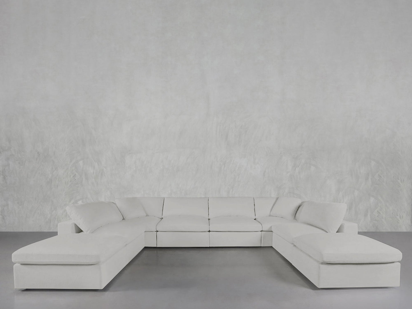 The 8-Seat Modular Double Lounger U-Sectional in white sits on a gray floor against a textured light gray wall, offering a modern and spacious minimalist interior style.