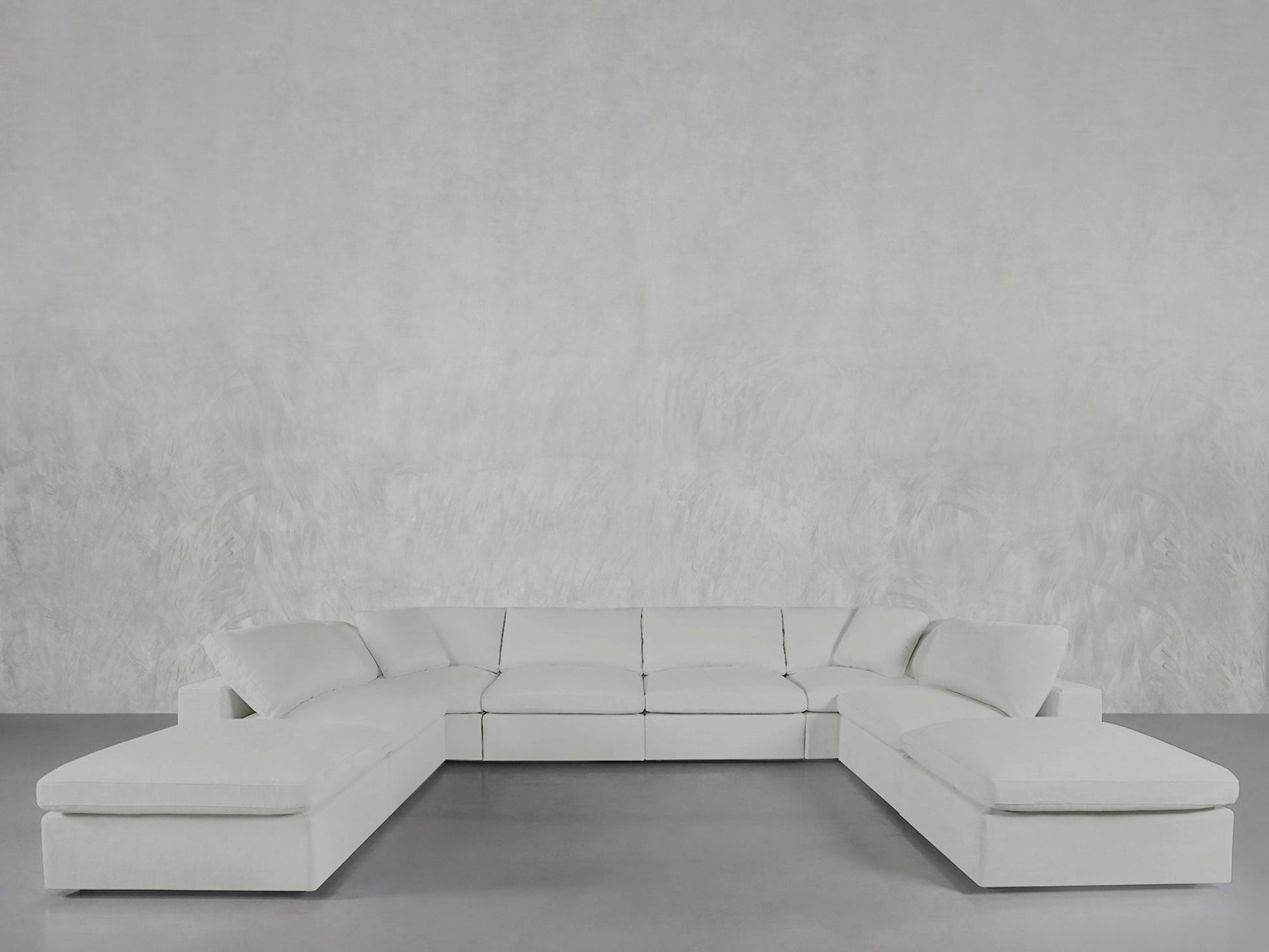 The 8-Seat Modular Double Lounger U-Sectional in white sits on a gray floor against a textured light gray wall, offering a modern and spacious minimalist interior style.