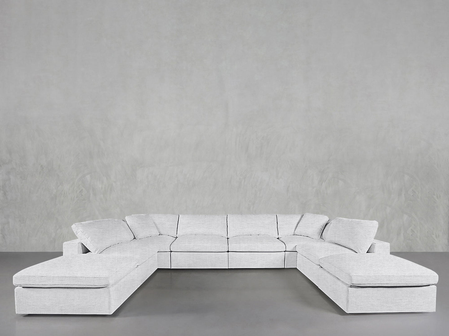 The 8-Seat Modular Double Lounger U-Sectional, in light gray, features wide cushioned seats and backrests, arranged in a minimalist room with matching walls and floors.