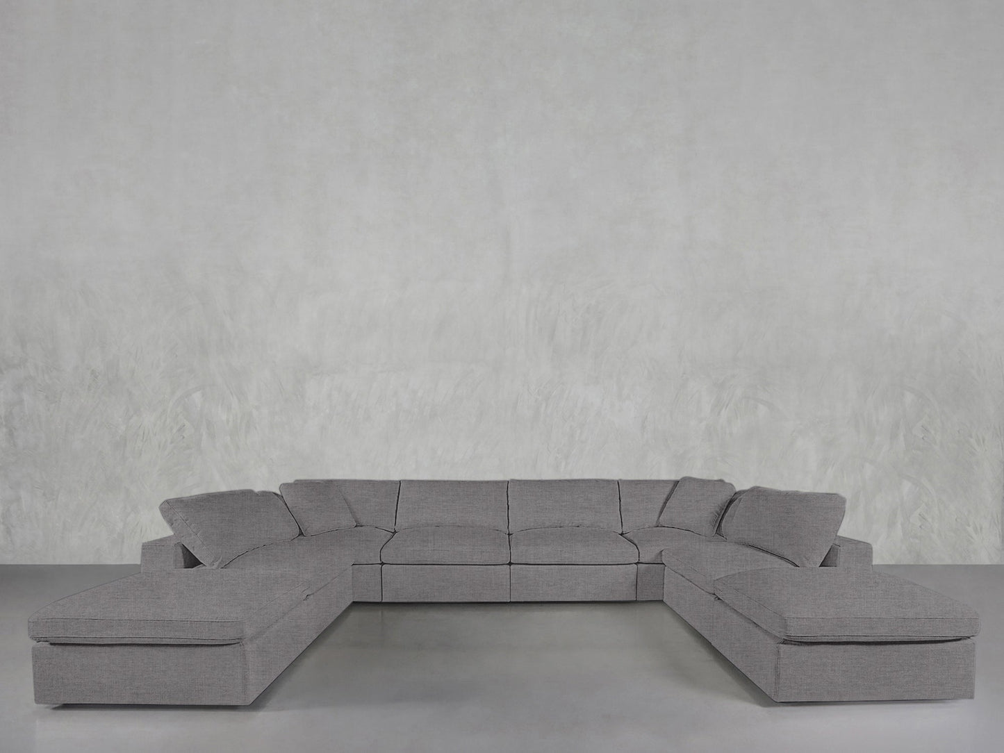 An 8-Seat Modular Double Lounger U-Sectional with wide seats and clean lines sits against a light gray textured wall on a smooth concrete floor.