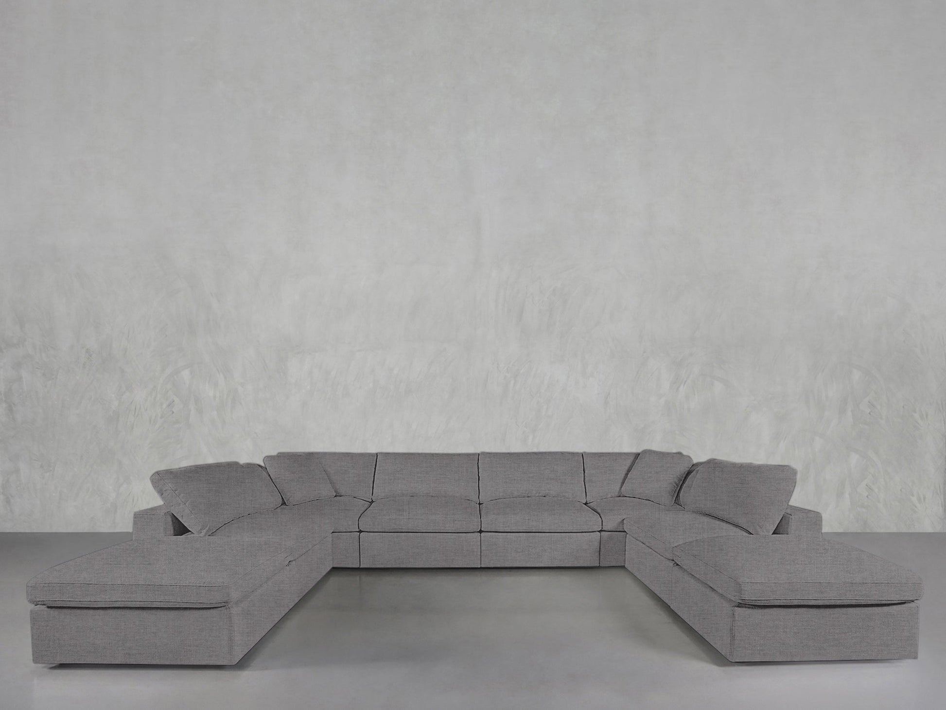 An 8-Seat Modular Double Lounger U-Sectional with wide seats and clean lines sits against a light gray textured wall on a smooth concrete floor.