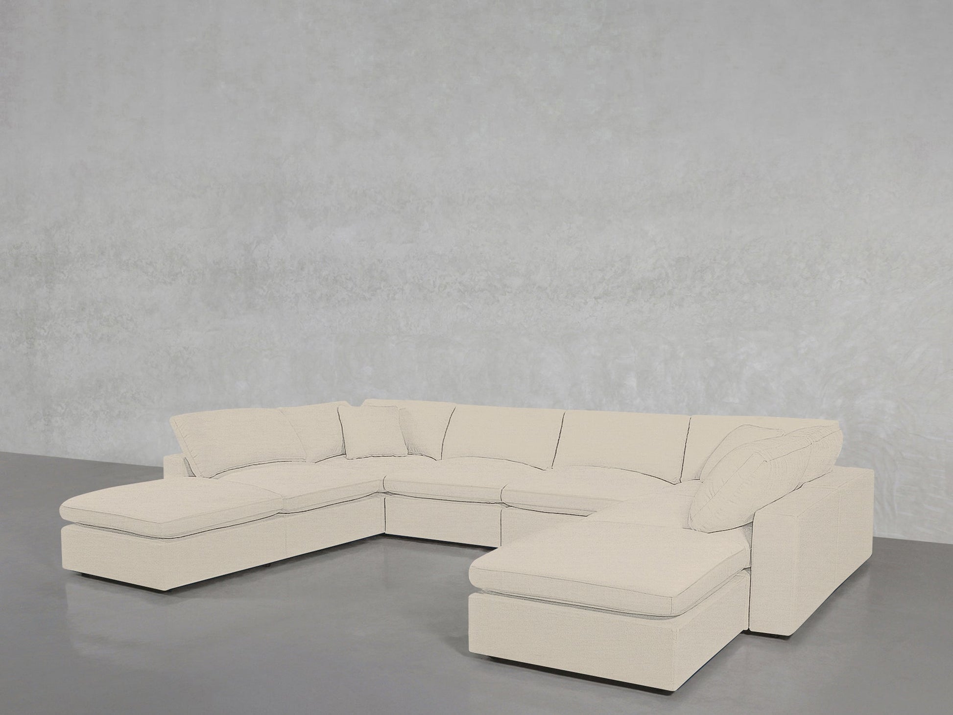 An 8-Seat Modular Double Lounger U-Sectional in beige with plush cushions sits in an empty room featuring a smooth gray floor and a lightly textured gray wall.