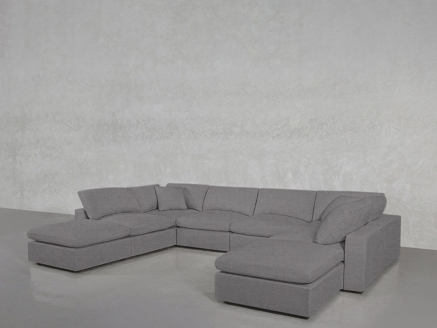 The 8-Seat Modular Double Lounger U-Sectional, in modern gray, features multiple seat and back cushions plus two accent pillows, arranged in a U-shape against a light-colored wall on a smooth floor.