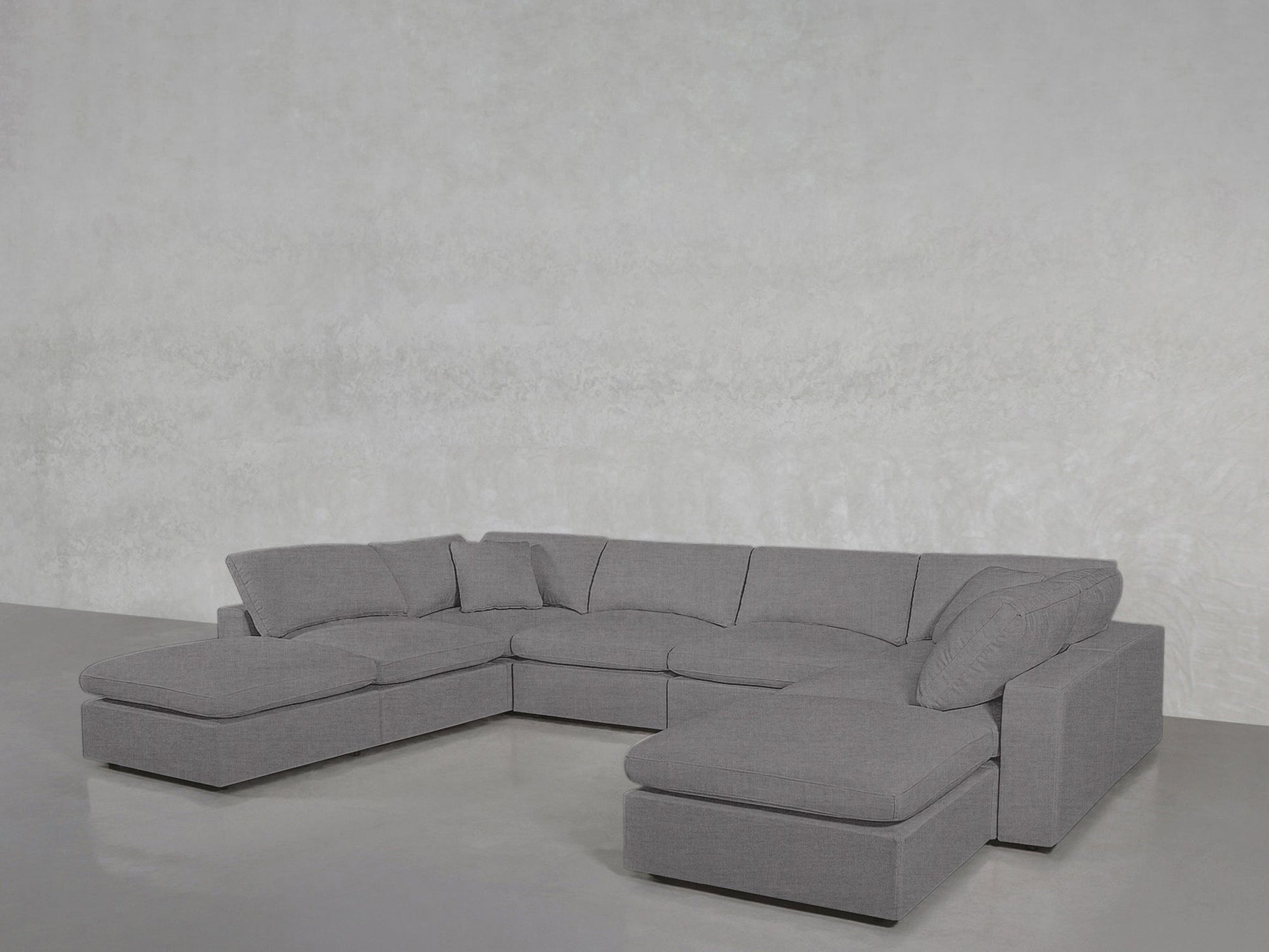 The 8-Seat Modular Double Lounger U-Sectional, in modern gray, features multiple seat and back cushions plus two accent pillows, arranged in a U-shape against a light-colored wall on a smooth floor.