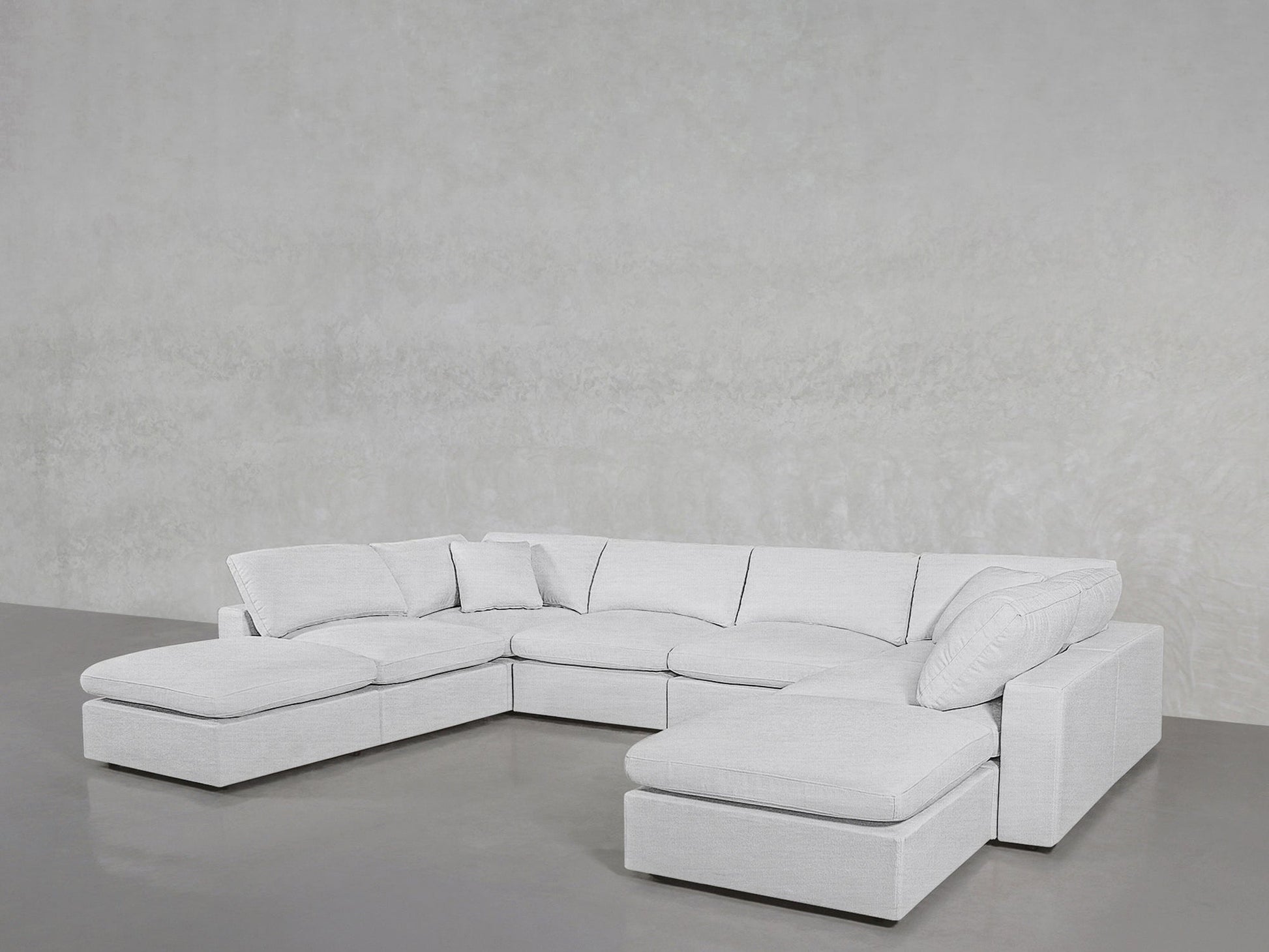 The 8-Seat Modular Double Lounger U-Sectional in light gray features multiple cushions and a chaise lounge, set against a textured light gray wall and smooth gray floor for a modern look.
