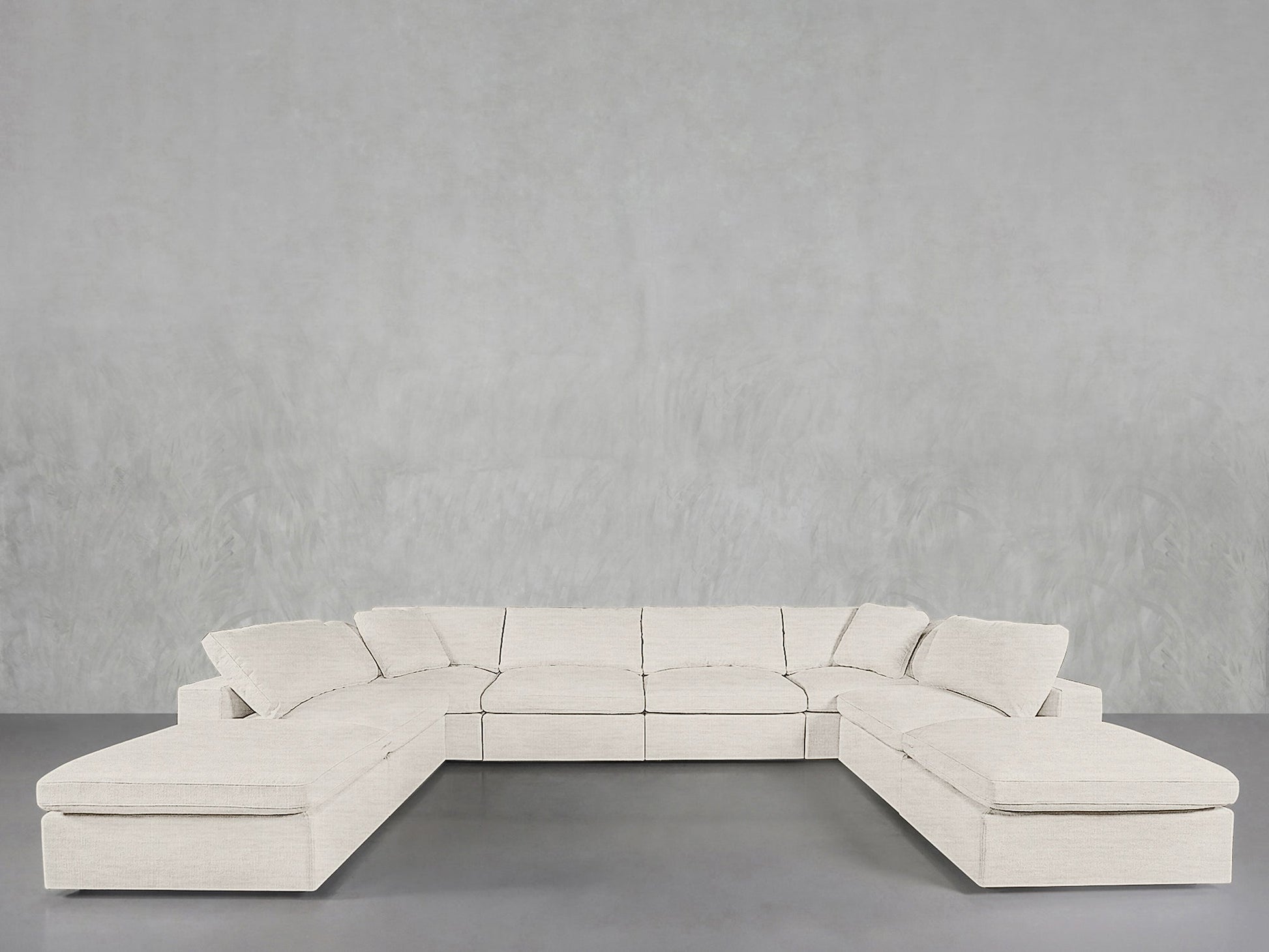 An 8-Seat Modular Double Lounger U-Sectional in light beige with cushions is arranged in a U-shape against a plain, light gray wall and smooth gray floor.