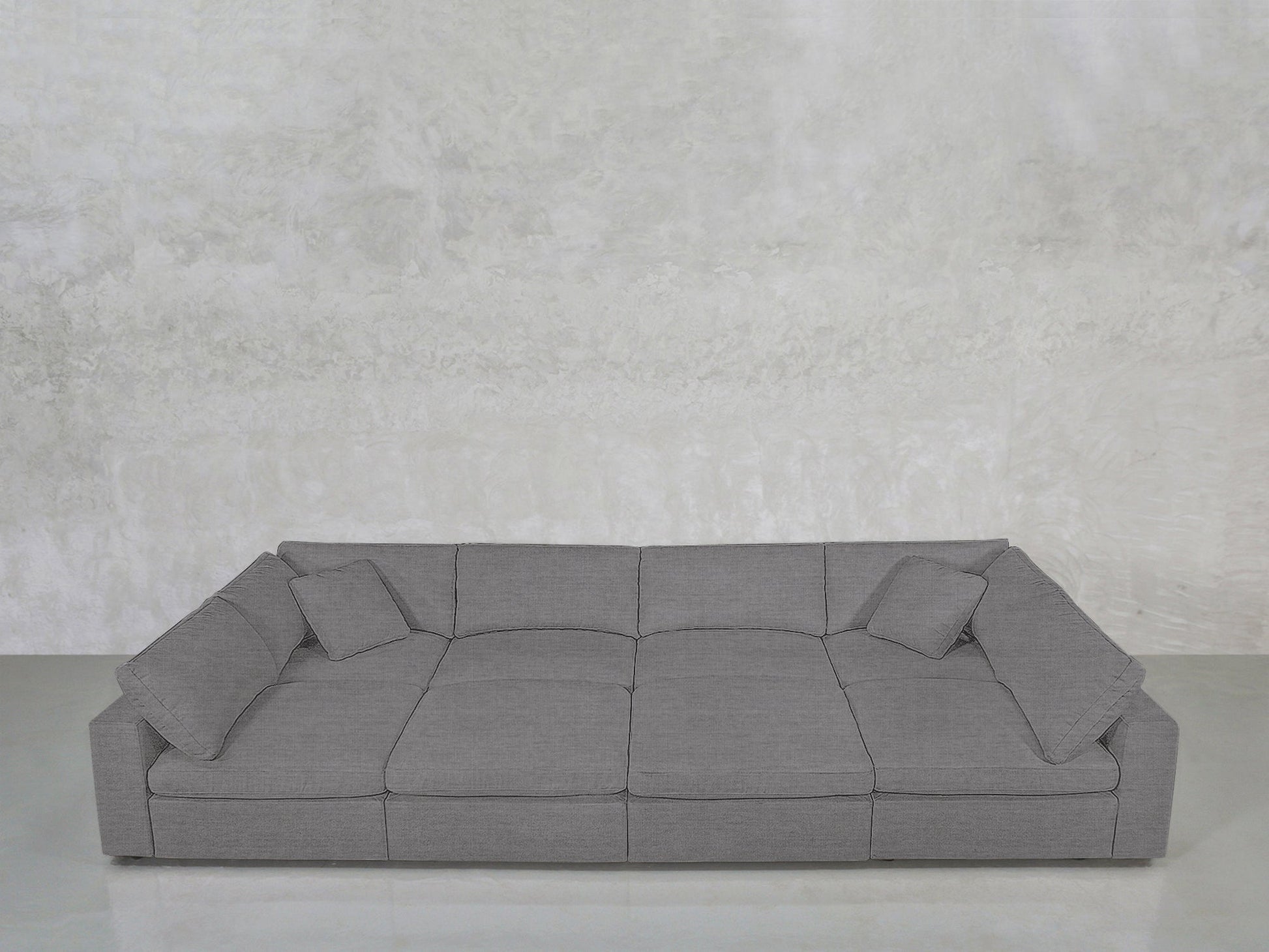 The 8-Seat Modular Pit features a modern grey design with three seat cushions, wide armrests, and four matching throw pillows, set against a light textured wall and floor.