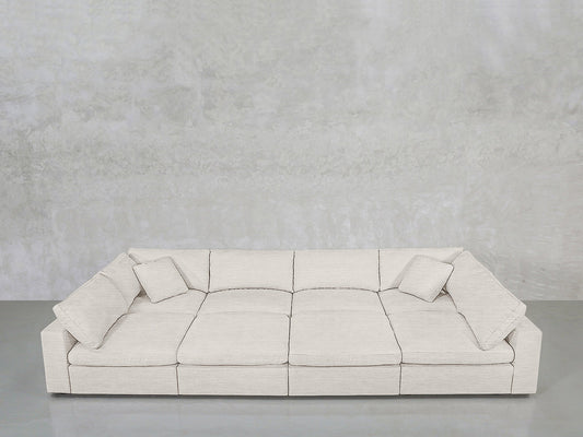 An 8-Seat Modular Pit in light gray, featuring three seat cushions and four matching throw pillows, sits against a textured light gray wall on a smooth gray floor.