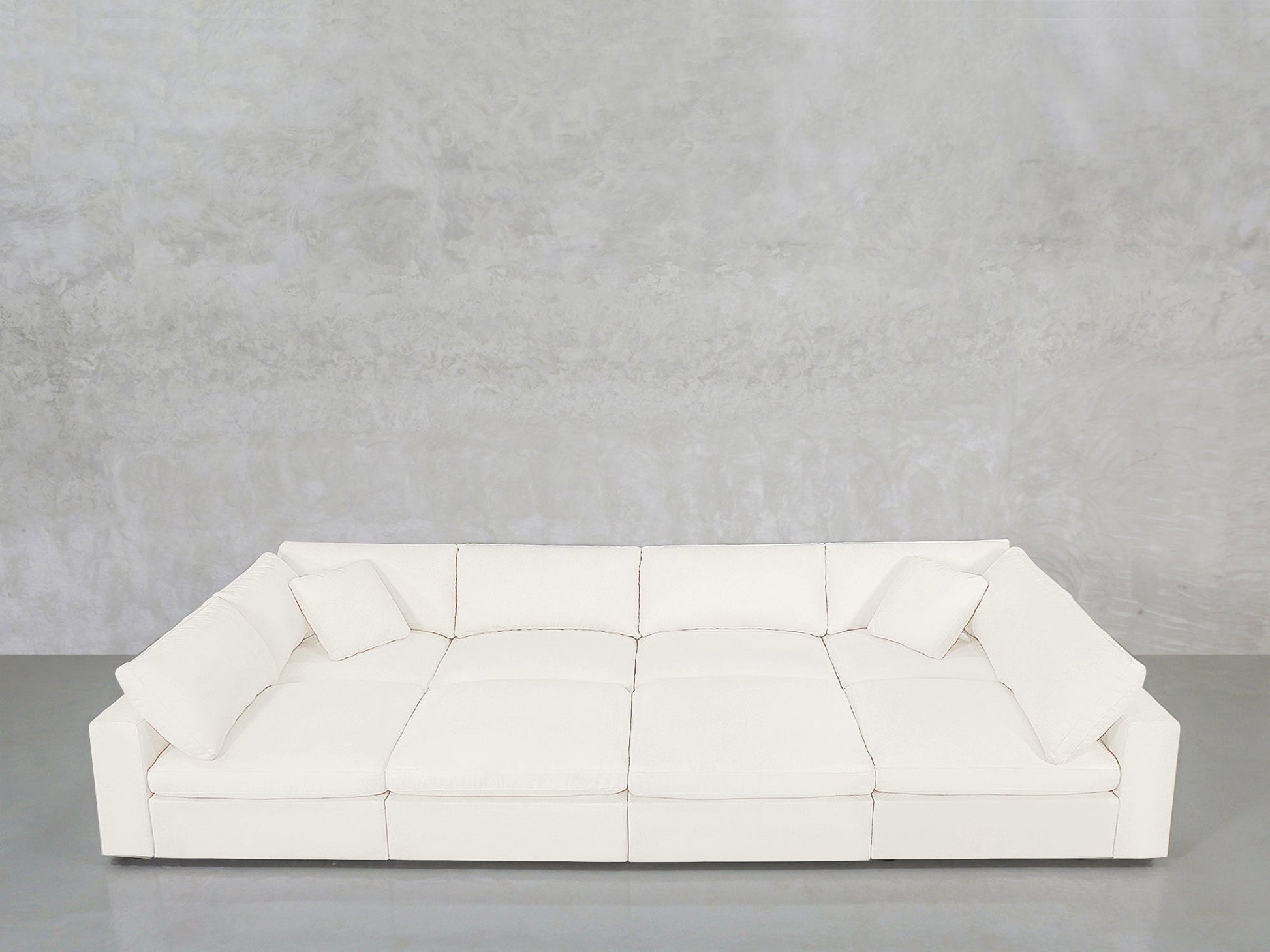 The 8-Seat Modular Pit features a modern white design with three seat cushions and four matching square pillows, set against a light gray textured wall and a polished gray floor.