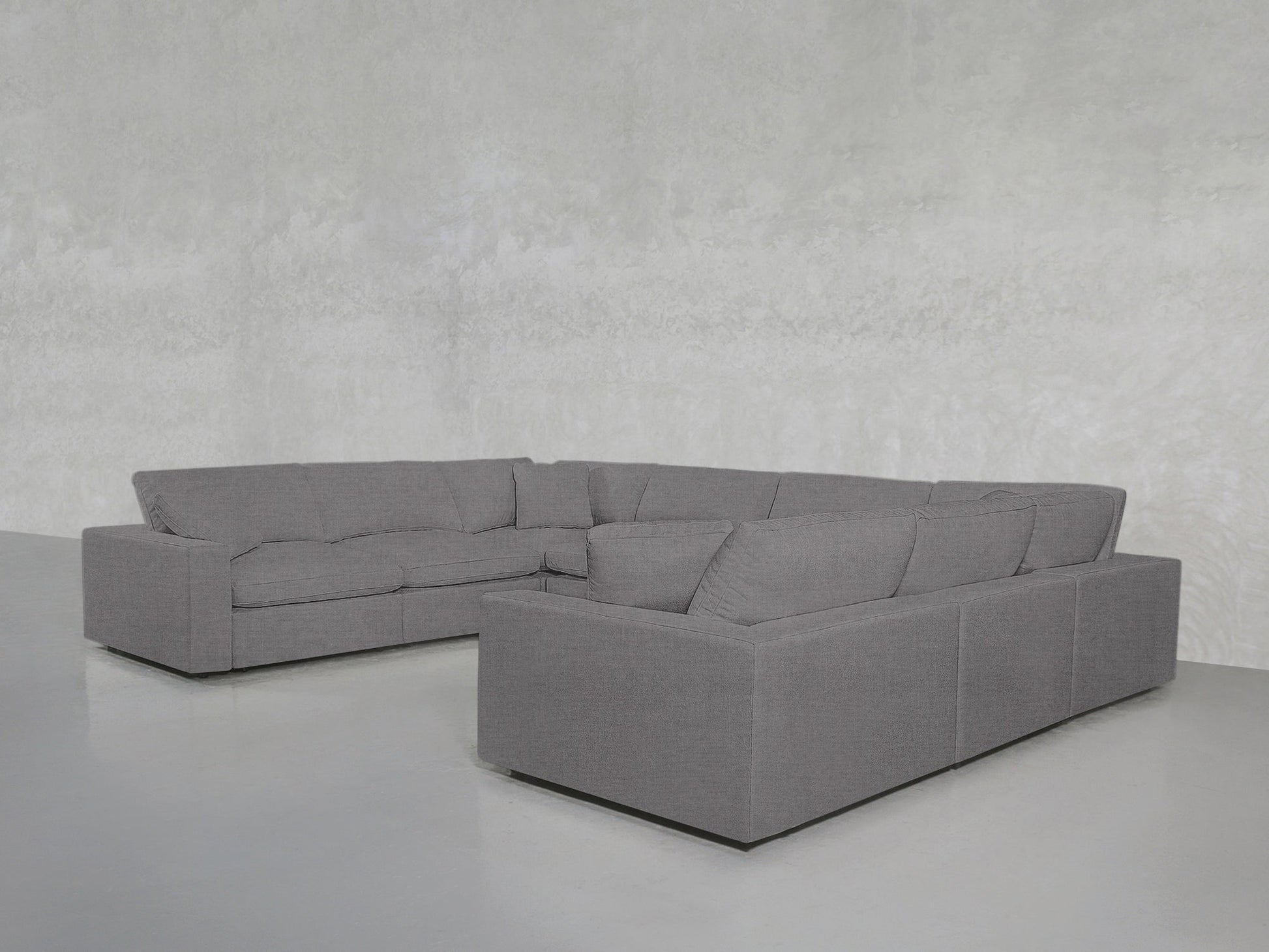 An 8-Seat Modular U-Sectional upholstered in light gray fabric is arranged in a minimalist room with pale gray walls and a smooth, light-colored floor.