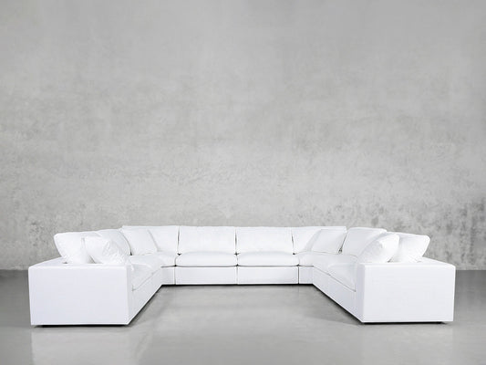 An 8-Seat Modular U-Sectional in white with cushions rests on a shiny, light gray floor against a plain, textured gray wall.