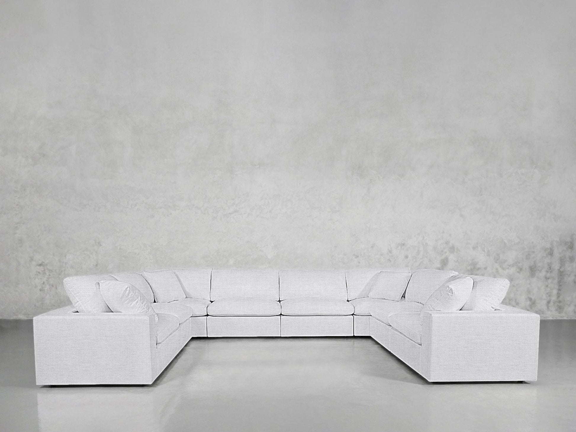 The 8-Seat Modular U-Sectional is a large, modern light gray sofa with multiple cushions, arranged in a U-shape against a textured gray wall and glossy floor.
