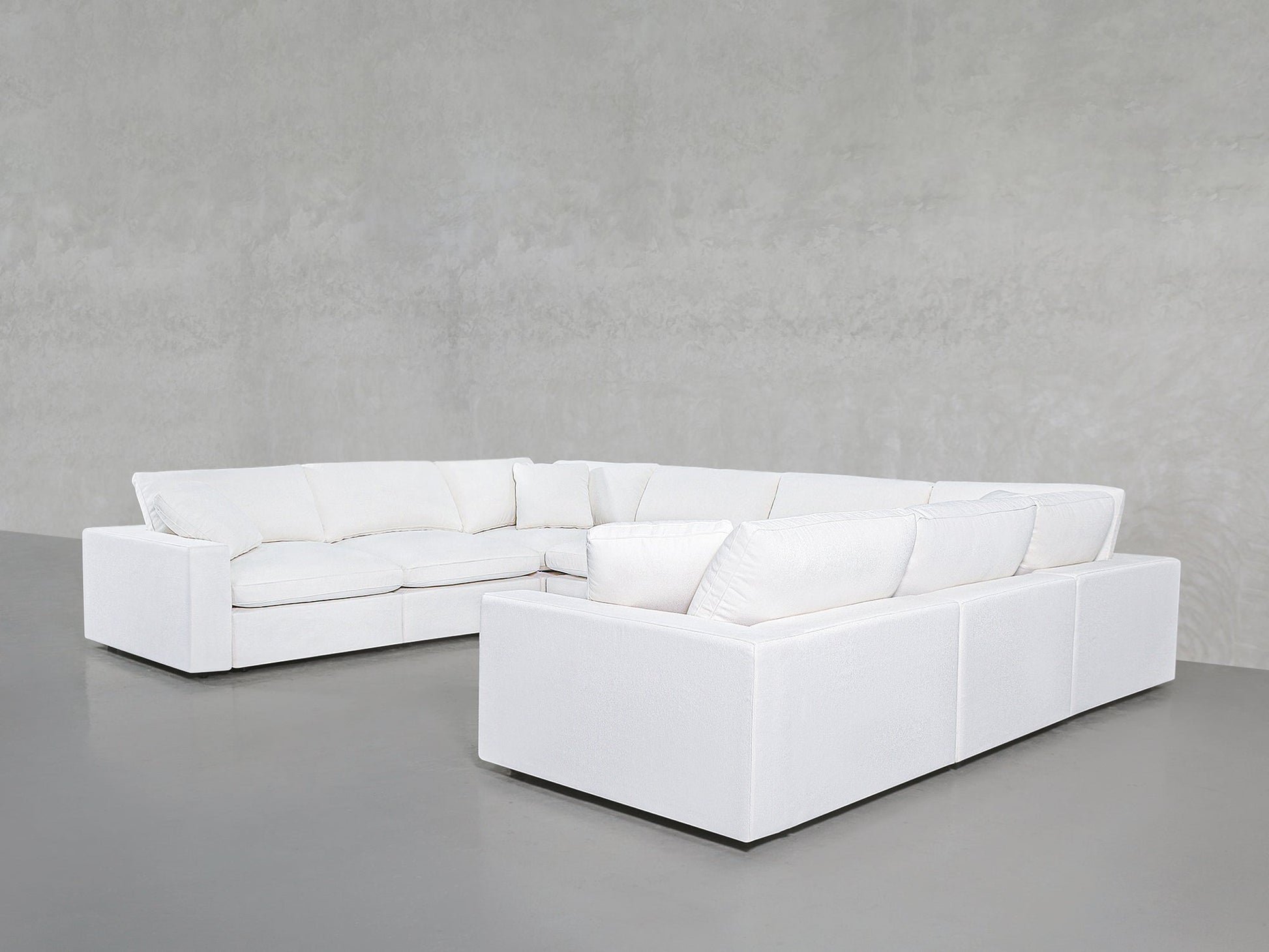 An 8-Seat Modular U-Sectional in modern white with deep cushions sits in the corner of a minimalist room with gray walls and a smooth gray floor.