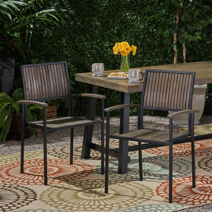 Two Vermilion Outdoor Dining Chairs with vertical slats and wooden arms sit on a colorful rug by a rectangular table topped with yellow flowers in a garden surrounded by greenery.