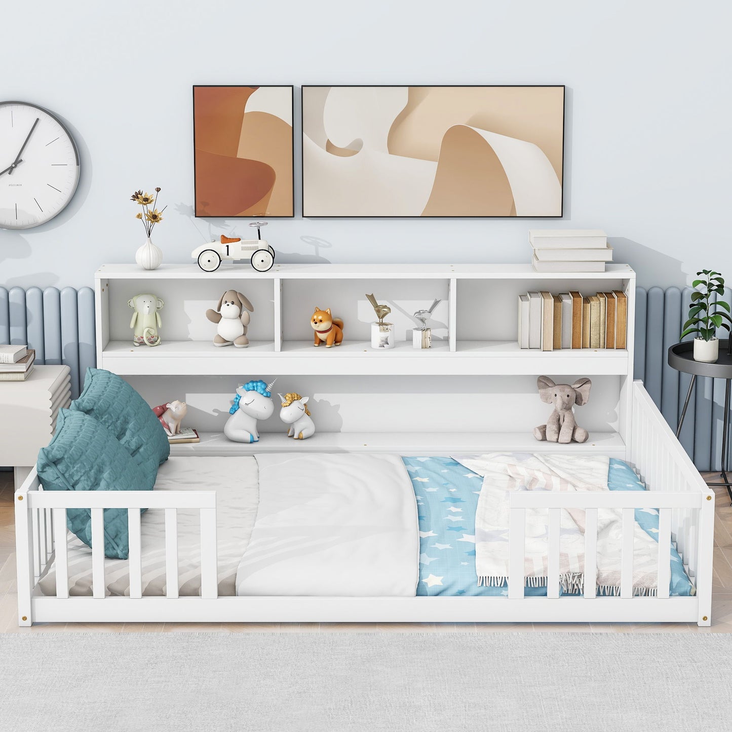 A Floor Bed With Side Bookcase, Shelves, and Guardrails is placed against the wall. Blue pillows and a star-patterned blanket add comfort, while toys, books, abstract art prints, a clock, and a plant decorate the space.
