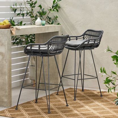 Two Outdoor Rattan Bar Chairs with metal legs and gray cushions stand by a concrete bar on a modern patio, complemented by green plants and a tan patterned rug.